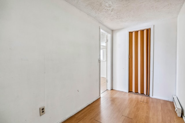 unfurnished room featuring a textured ceiling, a baseboard heating unit, and light hardwood / wood-style flooring