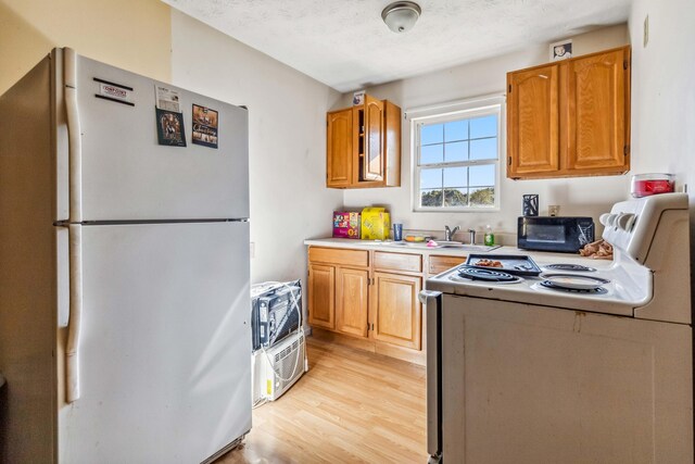 kitchen featuring a textured ceiling, sink, light hardwood / wood-style floors, and white appliances