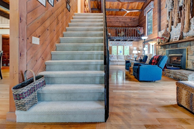 stairs featuring wood-type flooring, high vaulted ceiling, wooden ceiling, a stone fireplace, and wood walls