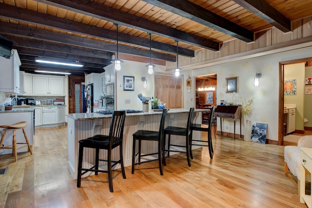 kitchen with light stone countertops, beam ceiling, decorative light fixtures, light hardwood / wood-style floors, and white cabinetry