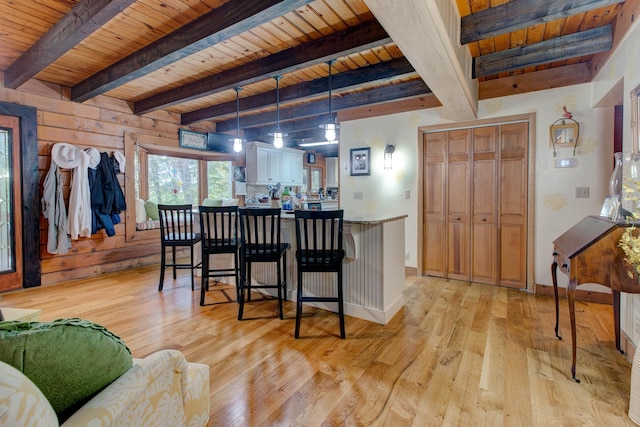 kitchen featuring beam ceiling, wood walls, hanging light fixtures, and light wood-type flooring