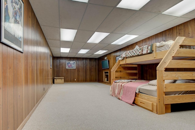 bedroom featuring a paneled ceiling, wooden walls, and light colored carpet