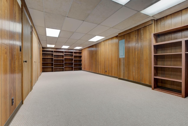 basement featuring a paneled ceiling, wood walls, built in shelves, and light carpet