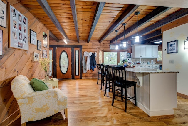 kitchen featuring pendant lighting, wood walls, light stone countertops, light hardwood / wood-style floors, and white cabinetry