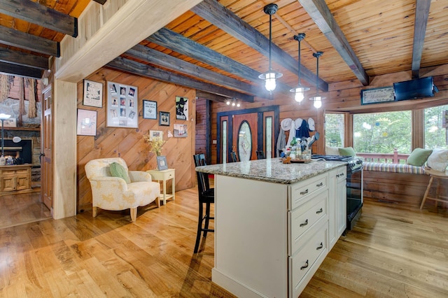 kitchen with beam ceiling, white cabinetry, hanging light fixtures, and wooden walls