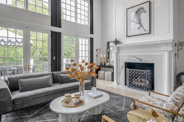 tiled living room with french doors, a high end fireplace, a high ceiling, and a wealth of natural light