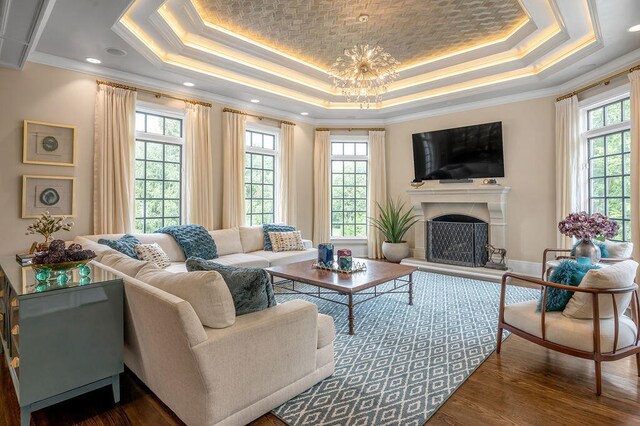 living room with a notable chandelier, ornamental molding, a tray ceiling, and dark wood-type flooring