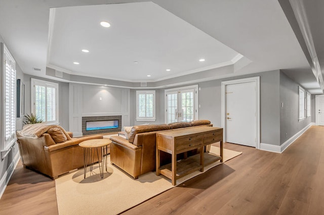 living room featuring a raised ceiling, ornamental molding, and light hardwood / wood-style flooring