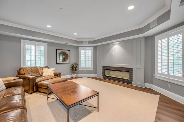 living room with a raised ceiling, ornamental molding, a tile fireplace, and hardwood / wood-style floors