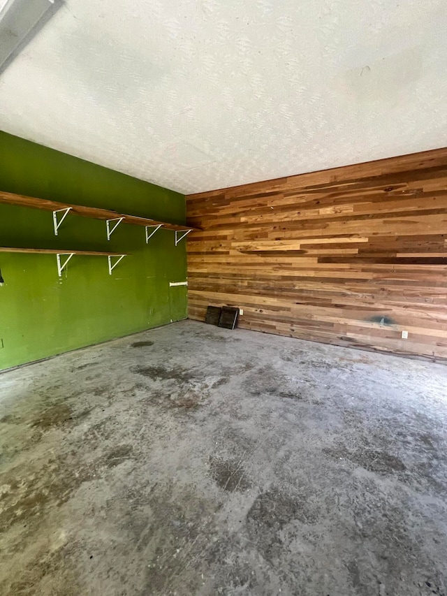 interior space with a textured ceiling, wooden walls, and concrete flooring