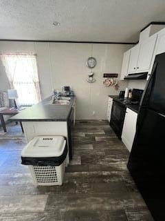 kitchen featuring a kitchen island with sink, black fridge, sink, a textured ceiling, and white cabinetry