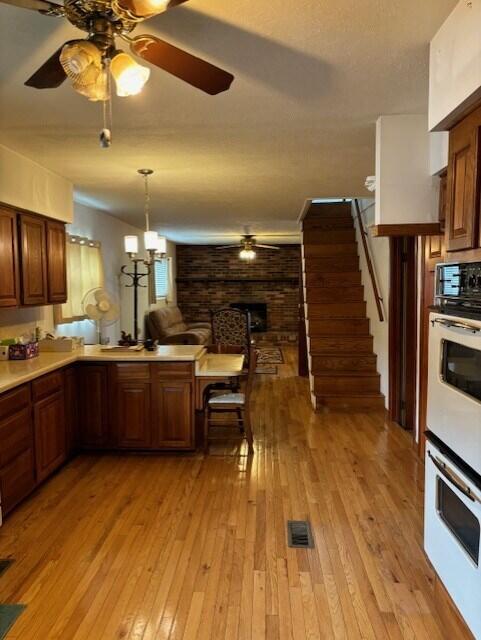 kitchen featuring decorative light fixtures, double oven, a fireplace, ceiling fan with notable chandelier, and light hardwood / wood-style floors