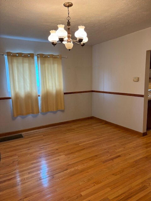 unfurnished room with an inviting chandelier, light hardwood / wood-style flooring, and a textured ceiling