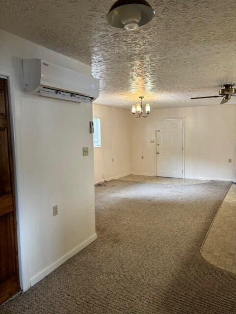 carpeted spare room with a wall unit AC, ceiling fan, and a textured ceiling