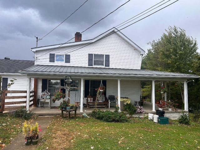 back of property featuring a yard, covered porch, metal roof, and a chimney