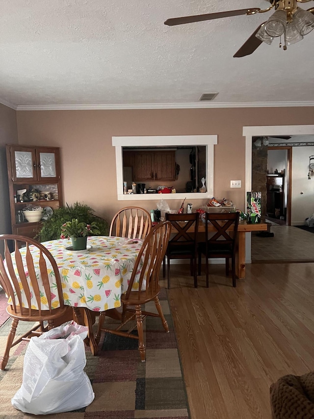 dining room featuring a textured ceiling, wood finished floors, visible vents, a ceiling fan, and ornamental molding