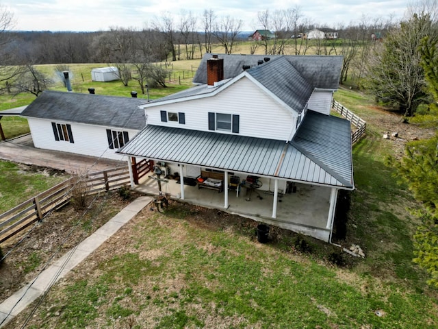 exterior space featuring a chimney, a lawn, a patio area, metal roof, and fence