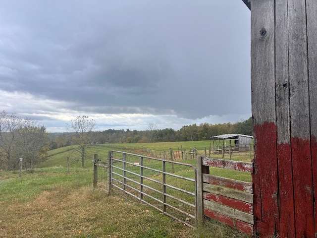 view of yard with a rural view, an outdoor structure, fence, and a gate