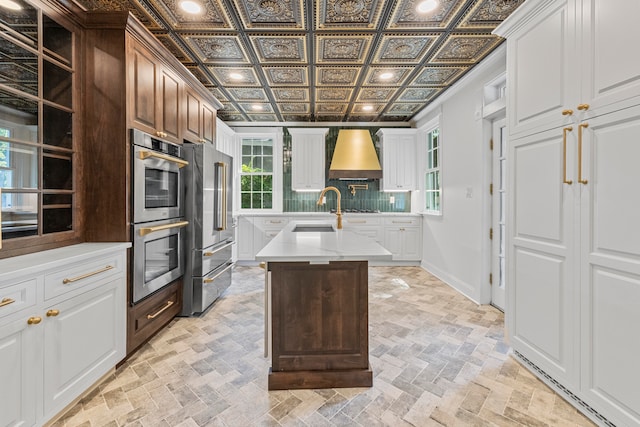 kitchen with stainless steel appliances, tasteful backsplash, white cabinets, sink, and a center island with sink