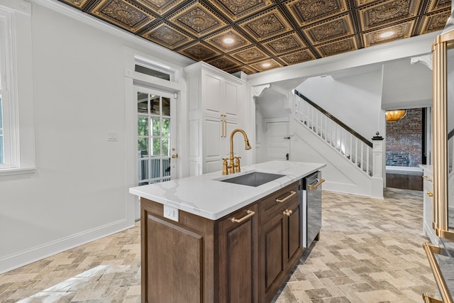 kitchen with dark brown cabinetry, white cabinets, light stone counters, sink, and a center island with sink