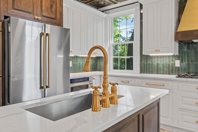 kitchen with stainless steel appliances, backsplash, premium range hood, and white cabinetry