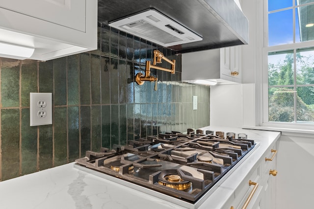 kitchen with range hood, white cabinets, tasteful backsplash, and light stone counters