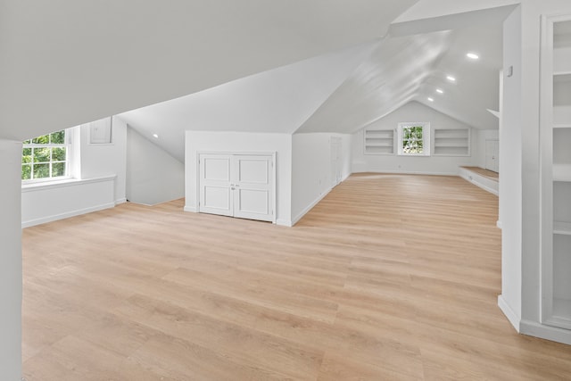 bonus room with built in shelves, vaulted ceiling, and light hardwood / wood-style floors