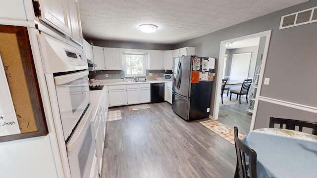 kitchen featuring sink, black appliances, light wood-type flooring, white cabinets, and a textured ceiling