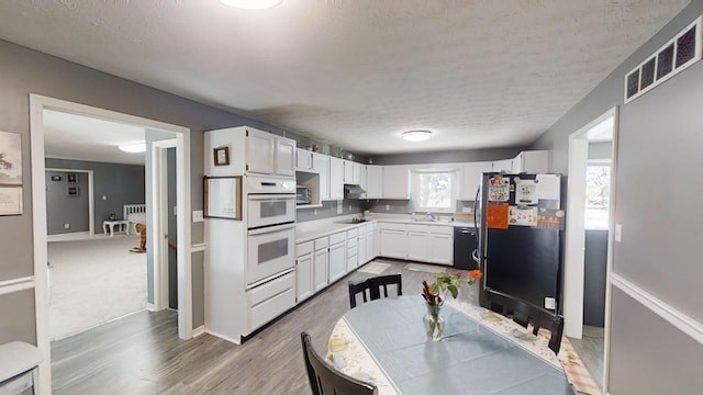 kitchen with wood-type flooring, sink, black appliances, white cabinetry, and a textured ceiling