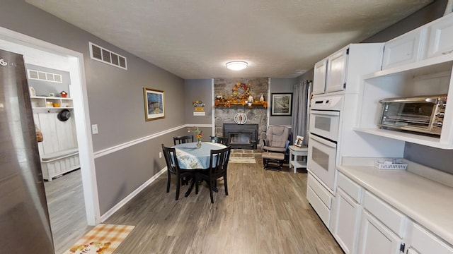 dining space featuring a stone fireplace, a textured ceiling, radiator heating unit, and light wood-type flooring