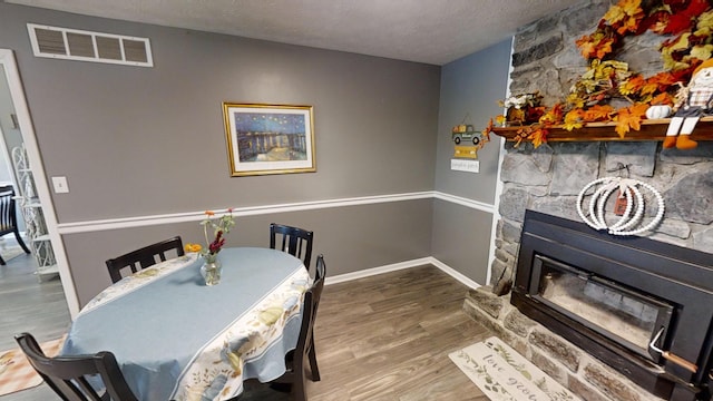 dining area with a textured ceiling, a stone fireplace, and wood-type flooring