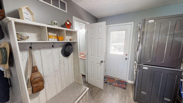 mudroom with a textured ceiling, stacked washer and clothes dryer, and light wood-type flooring