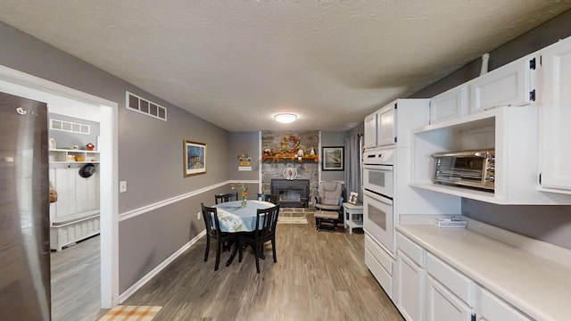 kitchen featuring a textured ceiling, white cabinetry, a fireplace, light hardwood / wood-style floors, and white double oven