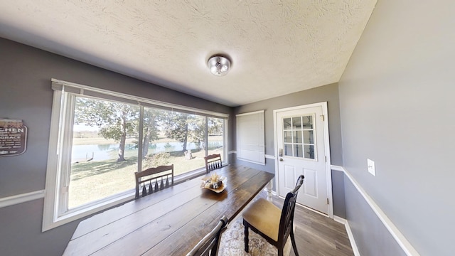 dining area featuring a textured ceiling, wood-type flooring, and a water view