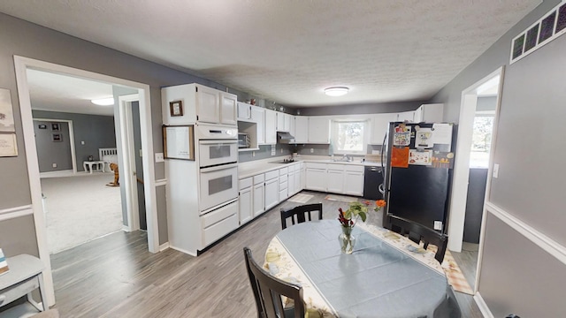 kitchen featuring black appliances, white cabinets, a textured ceiling, and light wood-type flooring