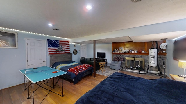 bedroom with a stone fireplace, water heater, and hardwood / wood-style flooring