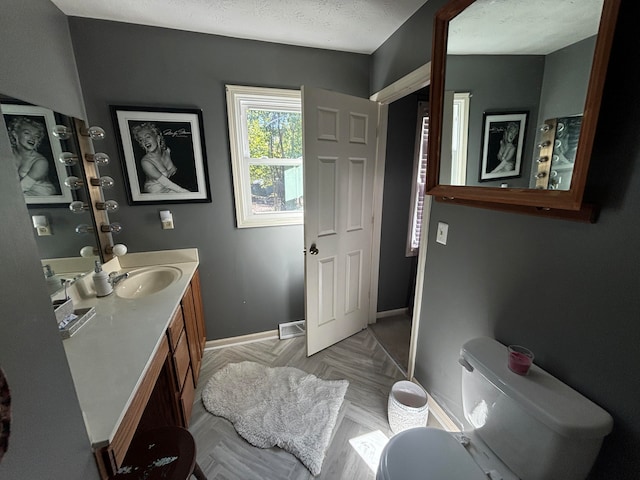 bathroom featuring parquet flooring, vanity, a textured ceiling, and toilet