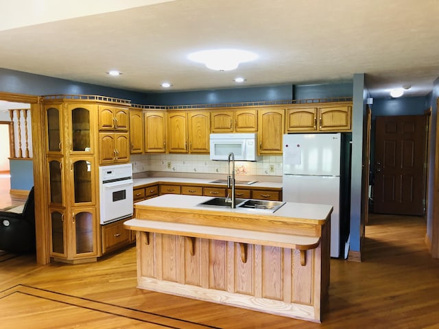 kitchen featuring tasteful backsplash, white appliances, light hardwood / wood-style floors, and a center island with sink