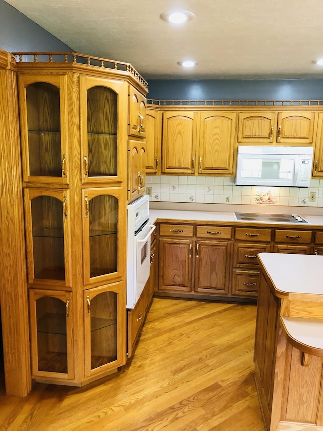 kitchen featuring light wood-type flooring, backsplash, and white appliances