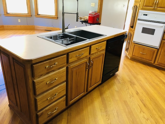 kitchen featuring dishwasher, sink, oven, a center island, and light wood-type flooring