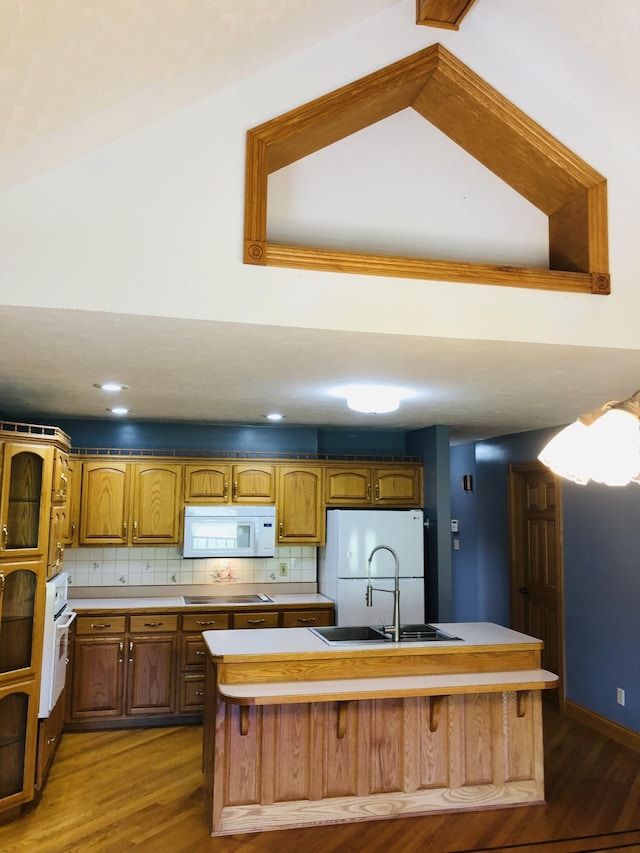 kitchen with hardwood / wood-style floors, tasteful backsplash, sink, a kitchen island with sink, and white appliances