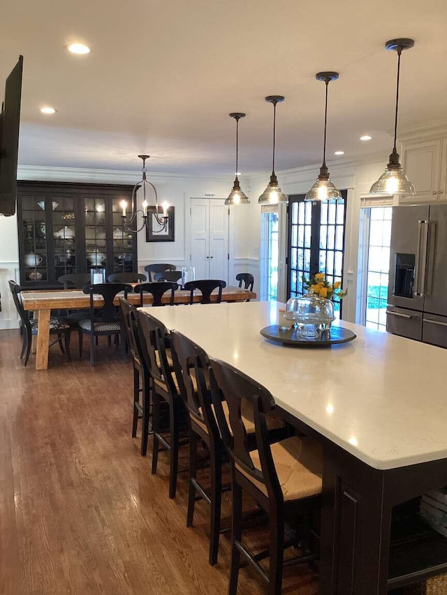 kitchen with high quality fridge, crown molding, a breakfast bar, dark wood-type flooring, and hanging light fixtures