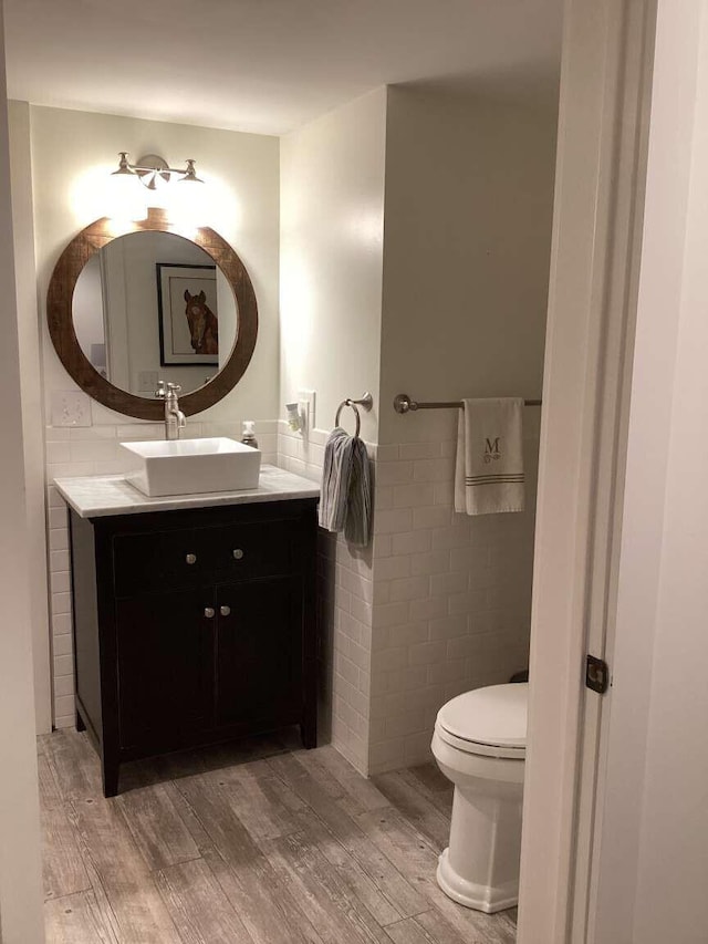 bathroom with tile walls, hardwood / wood-style flooring, vanity, and toilet