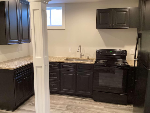 kitchen with light wood-type flooring, decorative columns, sink, light stone counters, and black appliances