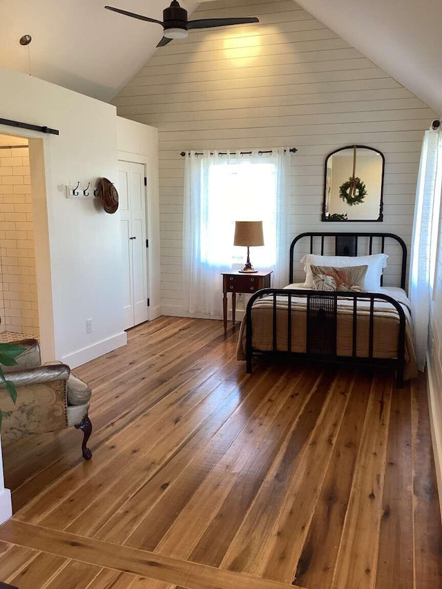 living area with wood-type flooring, a barn door, high vaulted ceiling, and ceiling fan