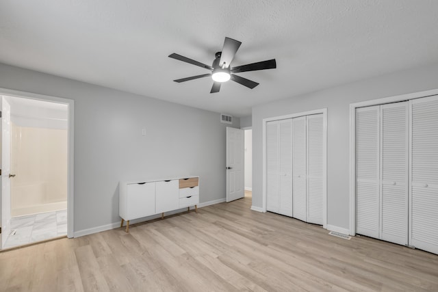 unfurnished bedroom with two closets, light hardwood / wood-style flooring, a textured ceiling, and ceiling fan