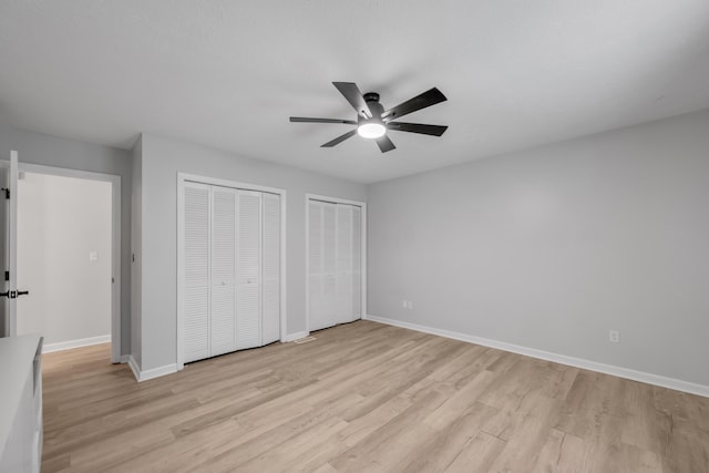 unfurnished bedroom with ceiling fan, light hardwood / wood-style flooring, and two closets