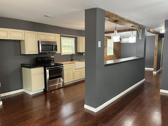 kitchen with cream cabinets, a sink, dark wood-type flooring, baseboards, and appliances with stainless steel finishes