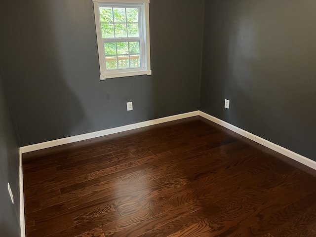 spare room with baseboards and dark wood-type flooring
