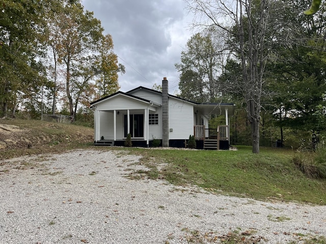 view of front of home featuring a chimney, a porch, and gravel driveway